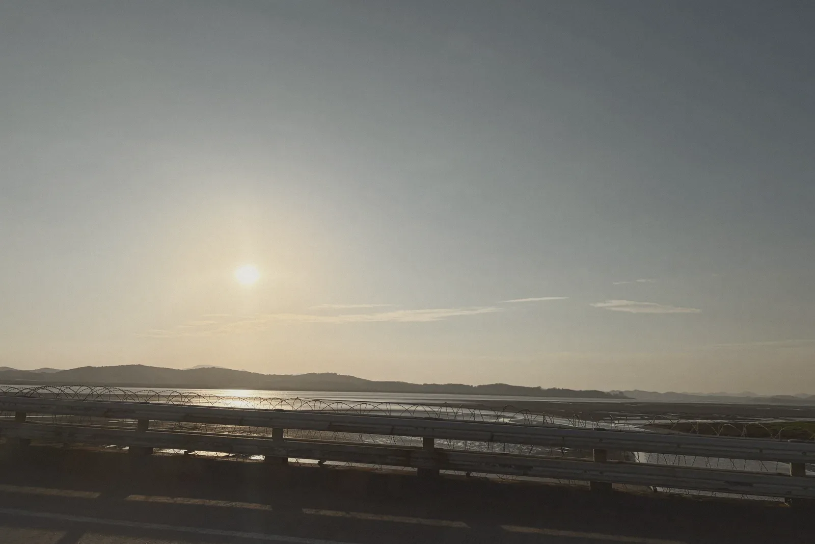 The sun low over open water, seen past a railing.