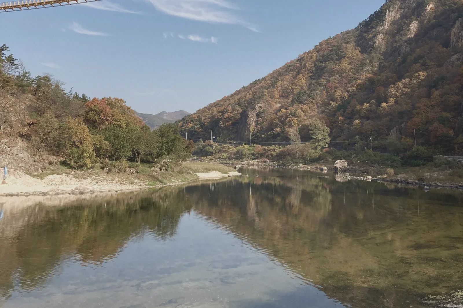 Autumn-coloured hills reflected in still water under a blue sky.