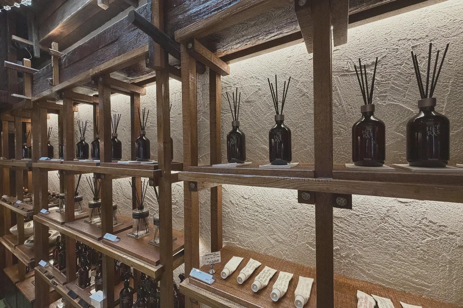 Amber glass reed-diffuser bottles lined up on a wooden shelf, lit from above.