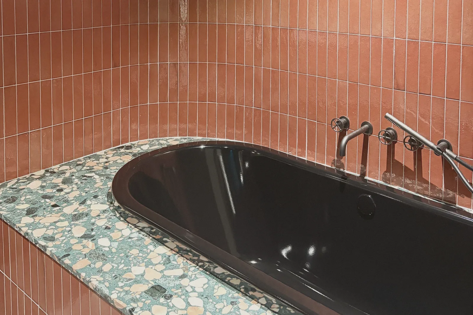 An orange-tiled bathroom wall with a wall-mounted faucet fixture.