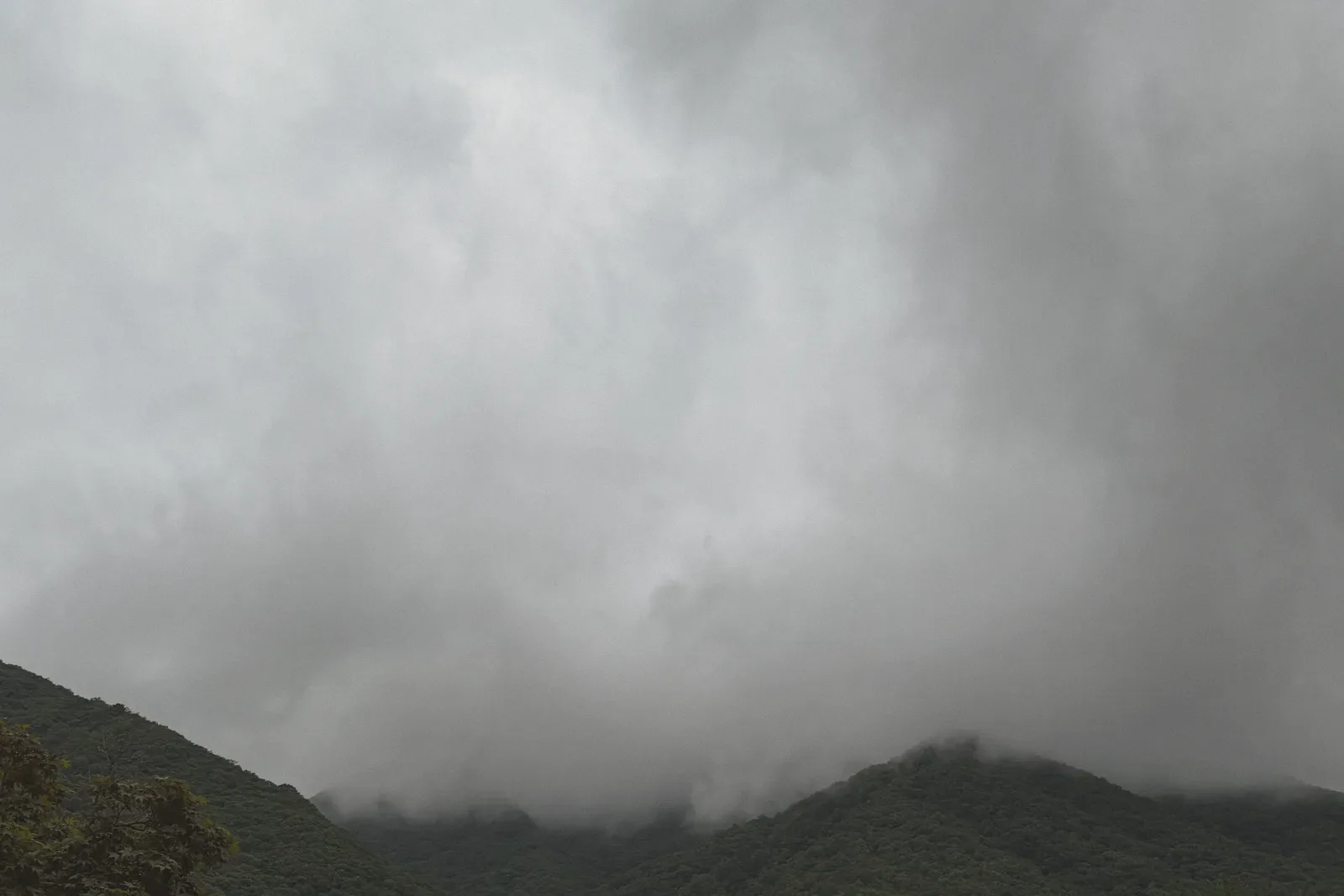 Heavy clouds rolling over layered green mountains.
