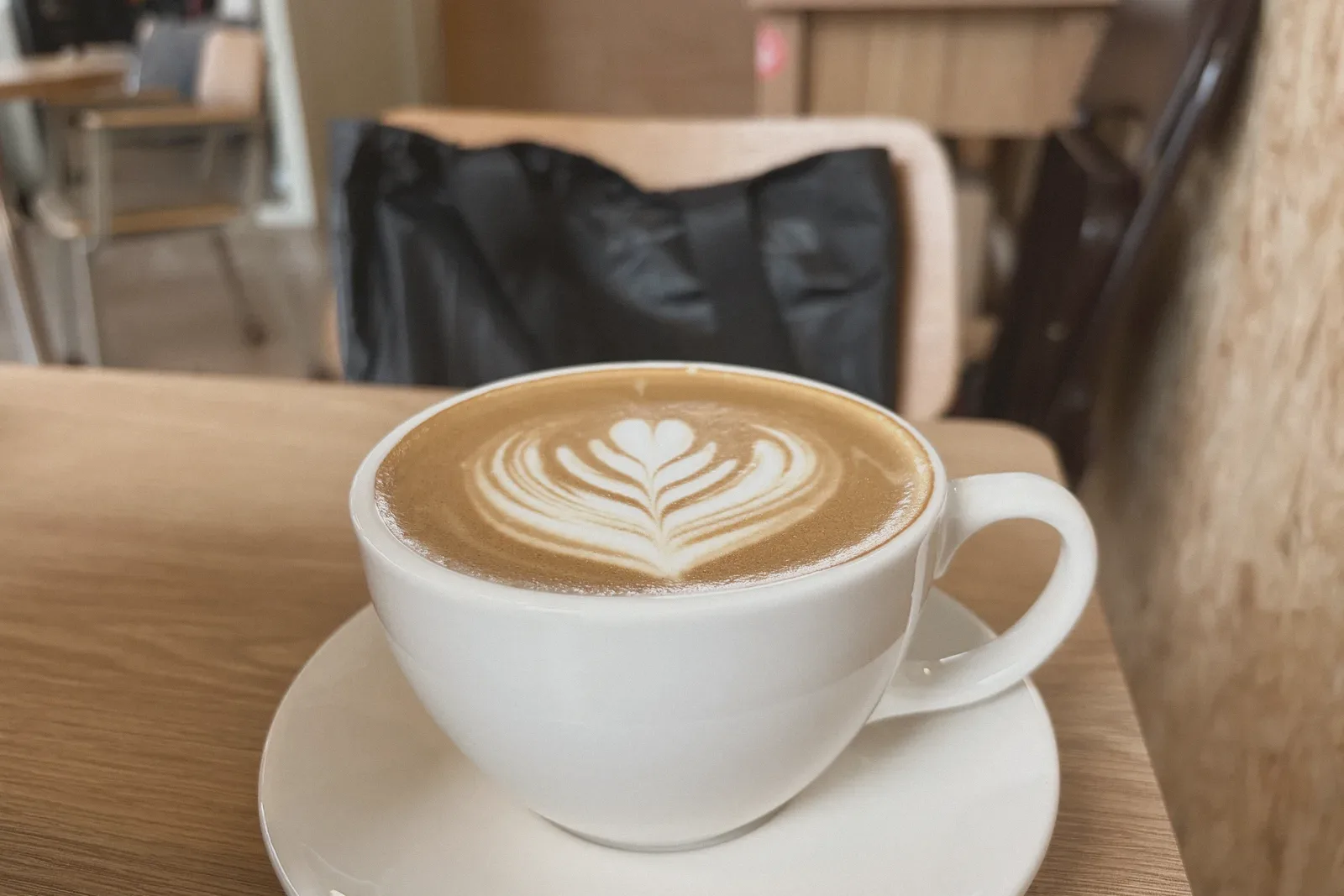 A cappuccino with leaf-patterned latte art on a wooden café table.