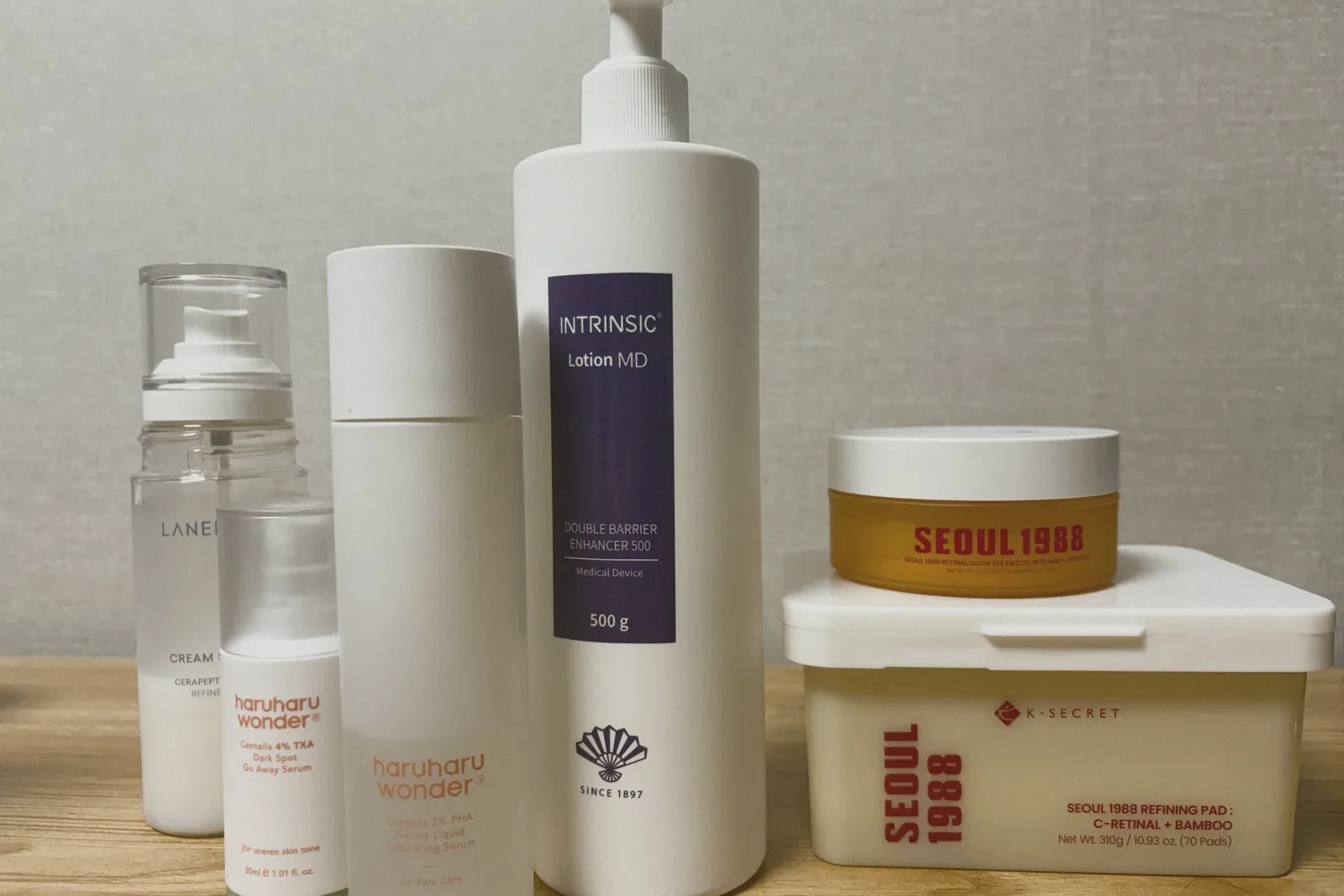 LANEIGE Cream Skin Refiner, two haruharu wonder serums, an Intrinsic Lotion MD pump bottle, and a SEOUL 1988 Refining Pad tub topped with a SEOUL 1988 Retinal Glow Eye Patch jar on a wooden table.
