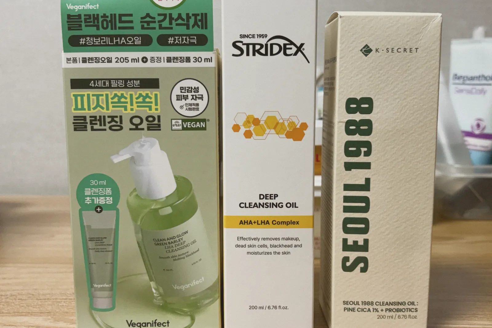 Three upright boxes of cleansing oil in a row: pale green, white with a yellow honeycomb pattern, and cream.