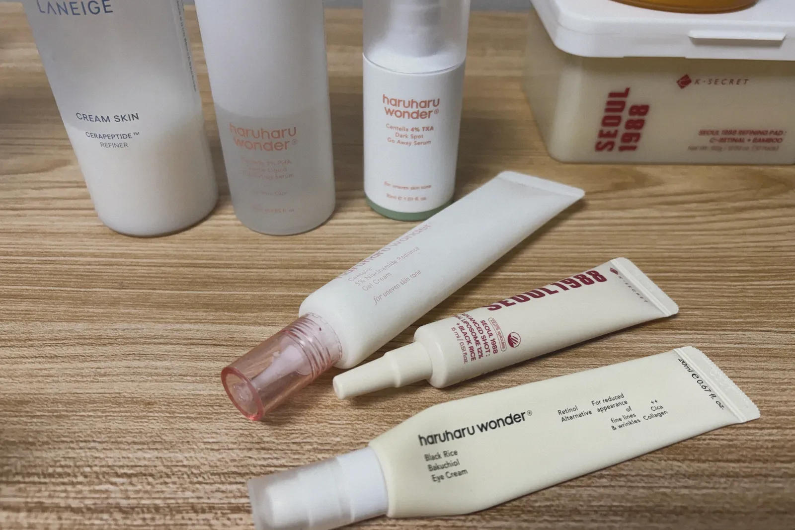 LANEIGE Cream Skin Refiner, two haruharu wonder serums, a haruharu wonder gel cream, a SEOUL 1988 Advanced Shot tube, a haruharu wonder Bakuchiol Eye Cream, and a SEOUL 1988 Refining Pad tub arranged on a wooden table.