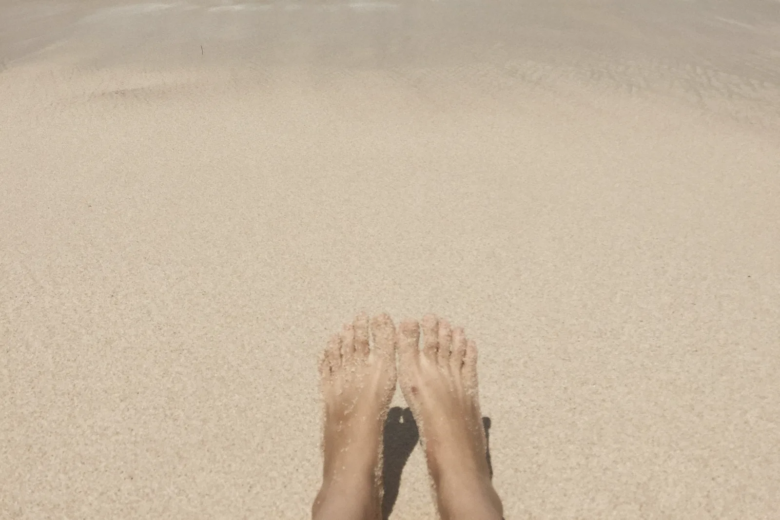 Bare feet resting on fine pale sand.
