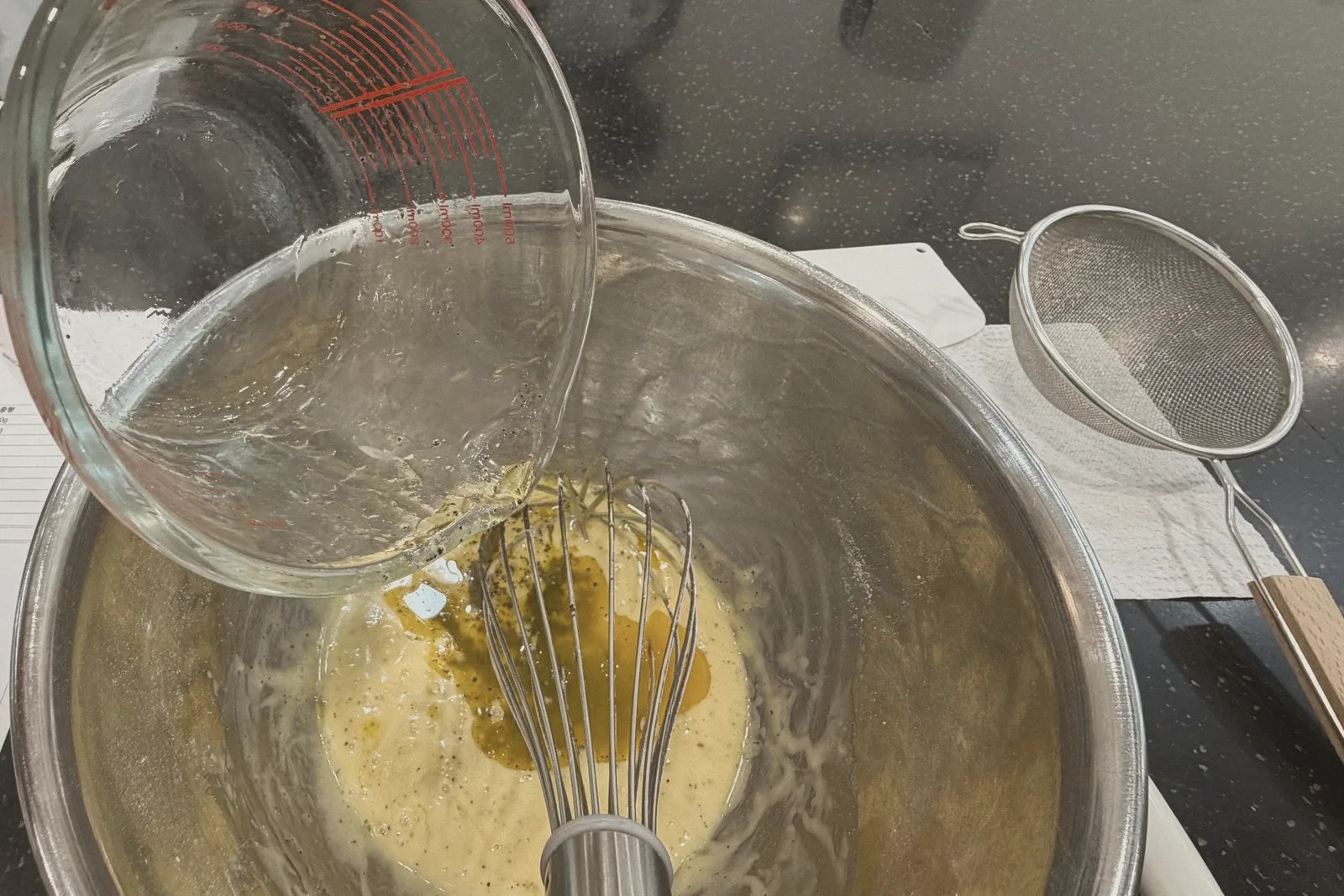 A whisk resting in a glass bowl of golden mixture.