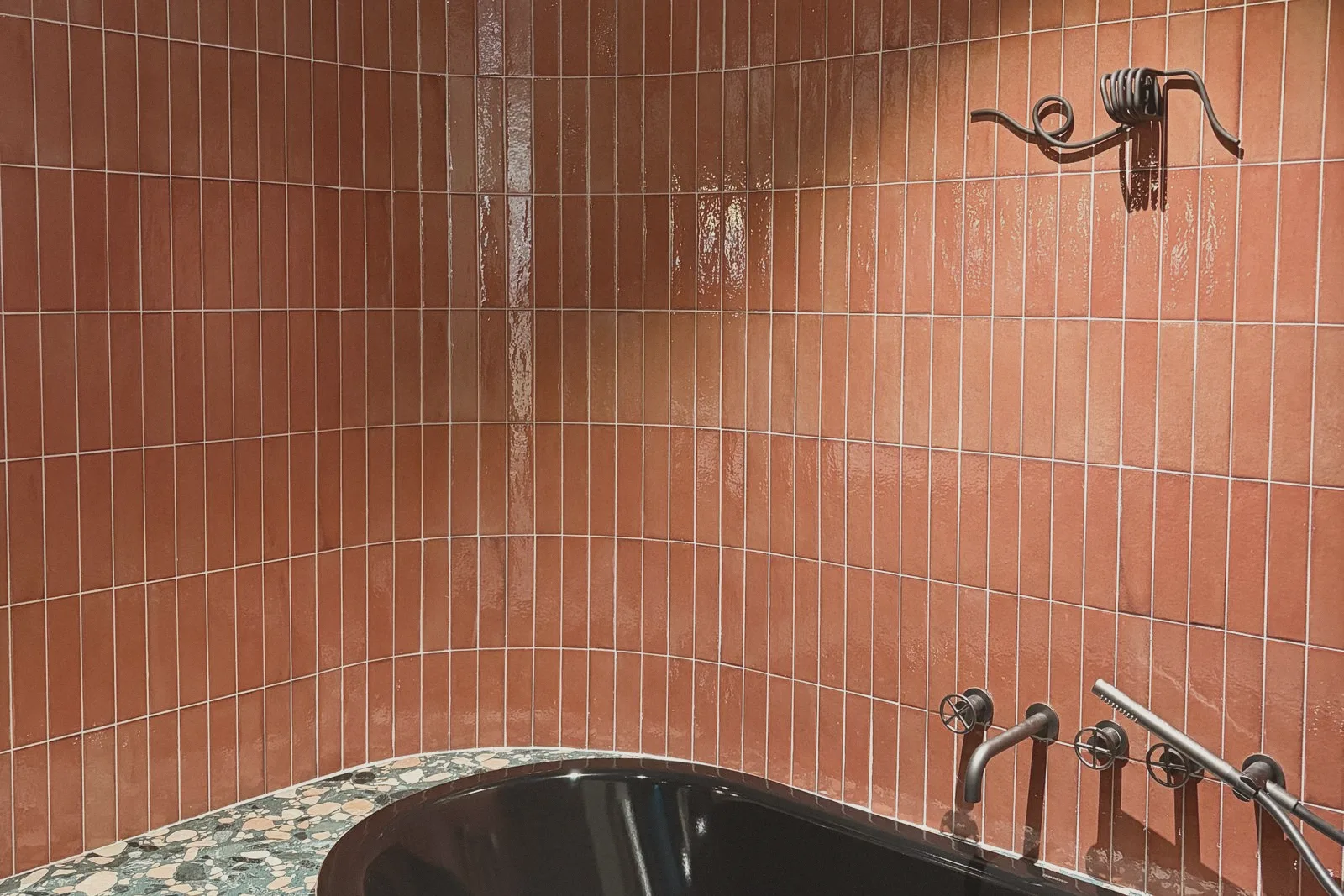 A dark bathtub set in terracotta tiles.